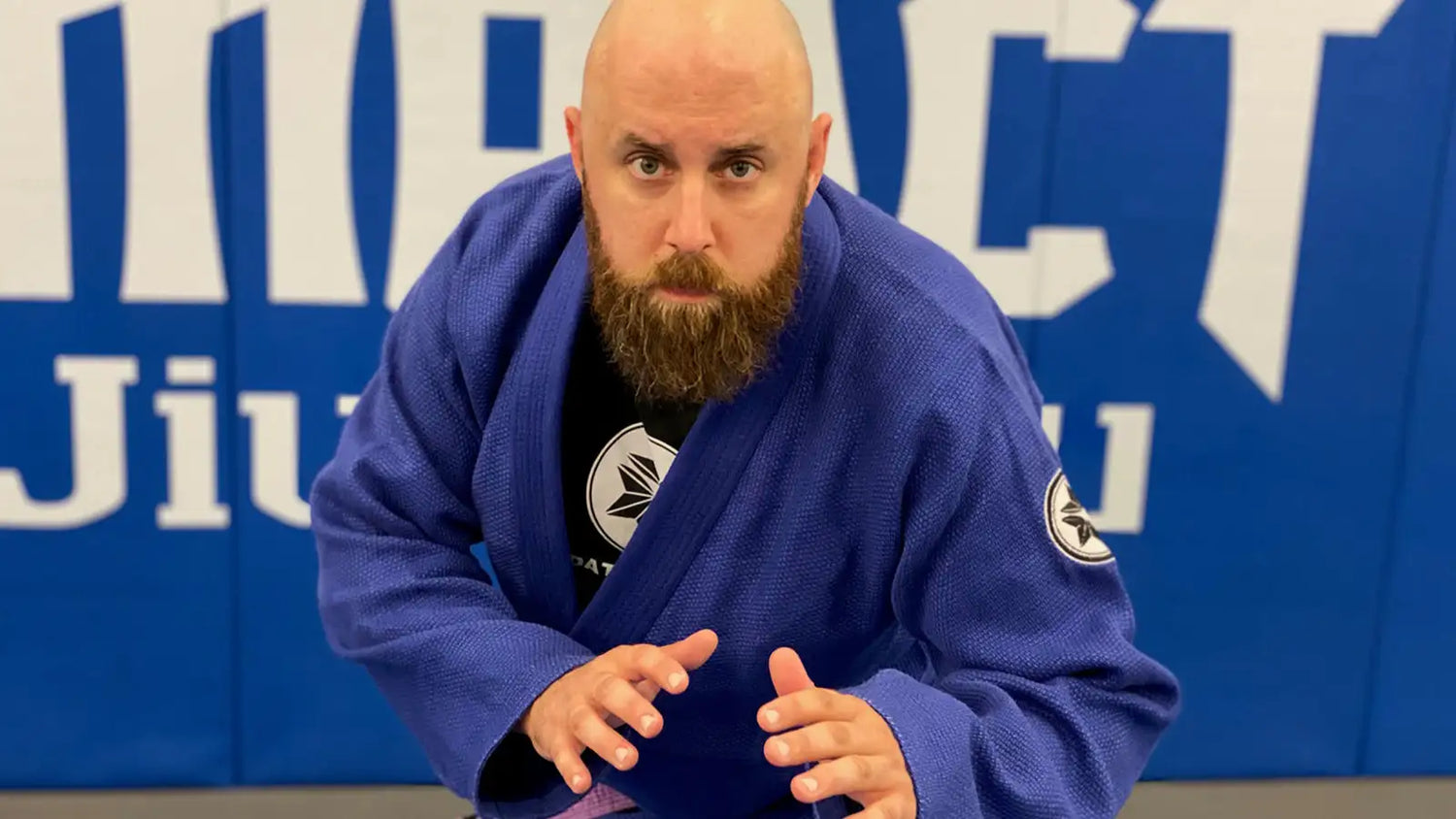 Man in a blue martial arts uniform posing in front of a blue banner with white text.